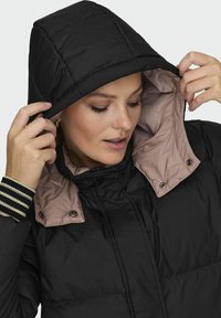 Svart polstret jakke med hette. Innvendig har den en lys pink fôr og stripete detaljer på ermene. Trykknapp- og glidelåsdetaljer.