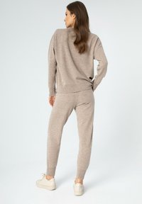 Beiger Strickpullover und passende Jogginghose aus weichem Material. Das Outfit hat eine lässige Passform mit gerippten Bündchen und wird mit hellen Sneakers kombiniert.
