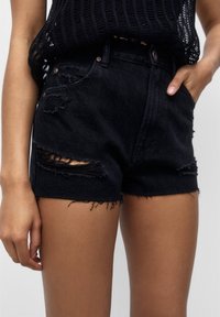 Shorts in denim nero con dettagli sfilacciati e orli sfrangiati. Presentano due tasche frontali e un design a vita alta.