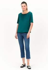 Teal satijnen blouse met een ronde hals, korte mouwen, gecombineerd met cropped blauwe denim jeans met knoopaccenten aan de zomen en zwarte instappers.