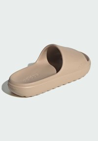 Beige halksandal gjord av slät plast med ett böjt rem och formad fotbädd. Har en logotyp präglad på ovansidan och en strukturerad sula.