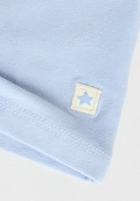 Lichtblauw katoenen t-shirt met een opgerolde zoom, waarop een klein, vierkant wit label is te zien met een geborduurde blauwe ster.