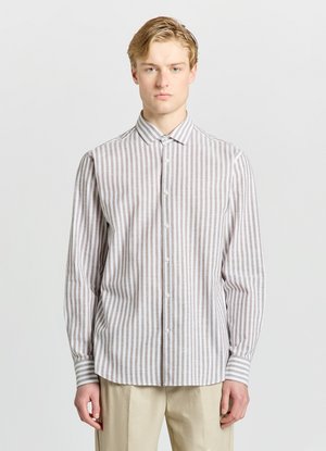 Man wearing beige and white vertical striped long-sleeve button-up shirt and light beige pants, standing against plain light background.