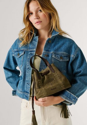 Junge Frau in Jeansjacke hält eine kleine olivgrüne Wildledertasche mit Ledergriffen und Quasten-Kordelzug.