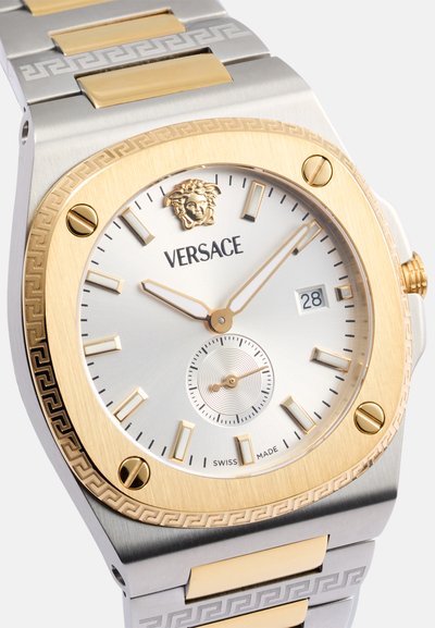 Orologio Versace con bracciale in acciaio inox argento e oro, quadrante rotondo, lunetta dorata, quadrante bianco e display della data alle 3. Sottodial circolare incluso.