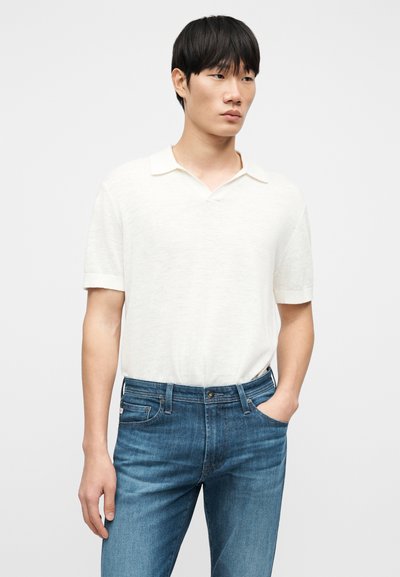 Μπλούζα πόλο σε ανοιχτό μπεζ λινό μείγμα με κοντά μανίκια και μαλακό γιακά, συνδυασμένη με σκούρο μπλε τζιν παντελόνια που διαθέτουν μπροστινή τσέπη.