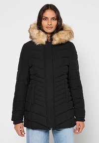 Doudoune noire avec capuche en fausse fourrure. Présente une texture matelassée en chevrons, une fermeture éclair frontale et des poches latérales. Coupe décontractée et matériau chaud.