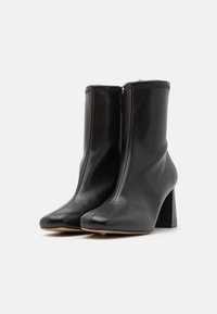 Bottines en cuir noir avec un bout pointu, un talon bloc et un design sans couture. Présente une fermeture éclair à l'arrière et une texture lisse.