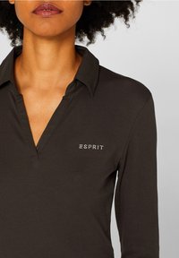 Polo a maniche lunghe in cotone marrone scuro con colletto. Presenta il logo "ESPRIT" in strass sul lato sinistro. Texture liscia.