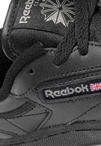 Reebok svart sneaker med teksturert overdel, polstret tunge og flate lisser. Utsmykket med logo og detalj av det britiske flagget.