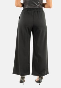 Pantalones de pierna ancha negros con cintura elástica y bolsillos laterales, fabricados en una tela lisa y ligera. Acentuados por unos tacones elegantes.