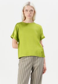 Satin green short-sleeve top with a relaxed fit and round neckline, paired with striped, loose-fitting trousers.