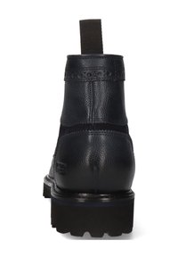 Botín de cuero negro hasta el tobillo con tirador, detalles de brogue en la parte superior y suela gruesa con relieve, mostrado desde la parte trasera.