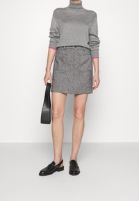 Grauer Rollkragenpullover mit pinken Ärmelabschlüssen, kombiniert mit einem grauen Tweed-Minirock und schwarzen Loafers, hält eine schwarze Tasche.