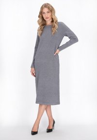 Rochie lungă gri, cu mâneci lungi, dintr-un material moale, cu decolteu rotund, buzunare laterale și mâneci cu nasturi. Este purtată cu pantofi cu toc înalt negri.
