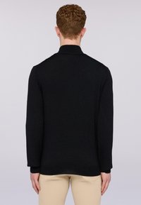 Černý pletený svetr s dlouhými rukávy a žebrovaným límcem. Má rovný střih a minimalistický design. Nosen s béžovými kalhotami.