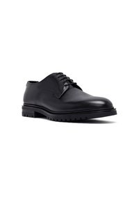 Zapato de vestir para hombre de cuero negro, con cordones, suela gruesa de taco, costuras visibles y punta redonda suave sobre fondo blanco.