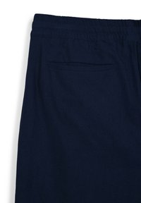 Marineblaue Hose mit elastischem Bund und einer einzelnen Gesäßtasche, gefertigt aus weichem Stoff. Glatte Textur, lockere Passform und schlichtes Design.