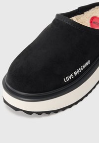 Črne semiš natikače z belo platformo. Imajo gumirani rob in bel "LOVE MOSCHINO" logotip na strani.
