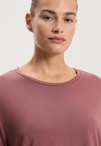 Tričko s krátkym rukávom a okrúhlym výstrihom vo tlmenej fialovej farbe, s hladkou textúrou a vo voľnom strihu, bez viditeľných vzorov alebo ozdôb.