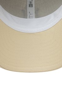 Beige Baseballcap mit einem weißen Schirm, ausgestattet mit einem strukturierten Stoff und einem Netzinnenfutter. Enthält ein Etikett mit Markeninformationen.
