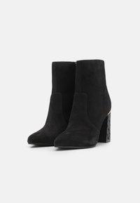 Bottines noires en suède avec un embout pointu et un talon bloc, présentant un design à motifs. La fermeture éclair est située à l'arrière.