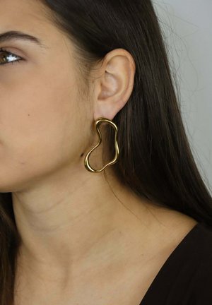 Orecchino astratto di forma dorata con un design intrecciato, appeso vicino all'orecchio, caratterizzato da superfici lisce e una finitura lucida.