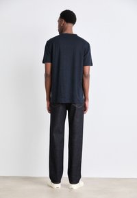 Camiseta de algodón navy con mangas cortas, combinada con pantalones de mezclilla oscuros. Textura sutil en la camiseta, corte casual y diseño liso. Zapatos con suela blanca.
