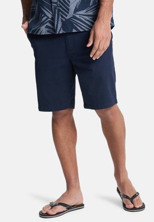 Pantalones cortos de color navy hechos de una tela ligera, con un corte recto y bolsillos laterales. Combinados con chanclas negras y una camisa estampada.