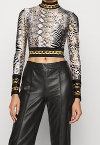 Long-sleeve crop top with animal print patterns in black, white, and gold, featuring a gold chain accent at the collar and waist. Paired with black leather pants.