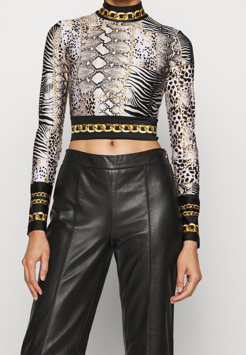 Long-sleeve crop top with animal print patterns in black, white, and gold, featuring a gold chain accent at the collar and waist. Paired with black leather pants.