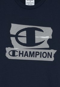 Marineblått stoff med hvit teksturert grafikk av Champion-logoen som har et stort "C" og teksten "CHAMPION" under.
