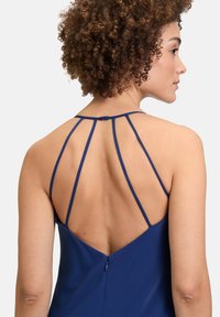 Robe bleu marine avec de fines bretelles réglables, un dos plongeant et une fermeture éclair. Tissu lisse avec un léger éclat et un design minimaliste.