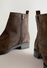 Pruunist suede'ist valmistatud pahkluu saapad krokodilliehnas, külgsete tõmblukkudega ja madala, plokknõelaga. Minimalistlik disain ümarate varvastega.