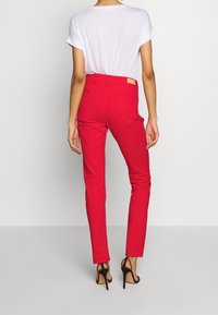 Pantalons rouges ajustés avec une texture lisse, une taille haute et de subtils poches arrière. Associés à un haut blanc à manches courtes.