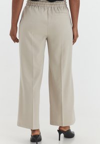 Beige, wijde broek met een elastische tailleband, een gladde textuur en een achterzak, gecombineerd met zwarte hakken.