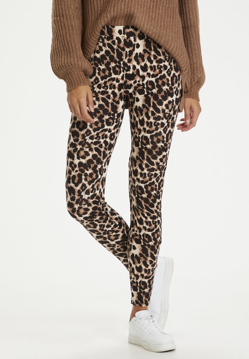 Leggings s leopard uzorkom u nijansama smeđe i crne, s prilagođenim dizajnom i mekom teksturom. Sparene s smeškastim pletenim puloverom i belim patikama.