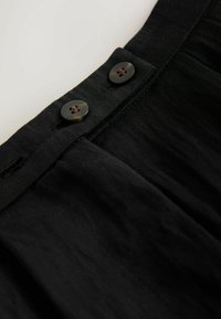 Fustă din țesătură neagră cu finisaj texturat, având doi nasturi rotunzi și închiși la culoare în zona taliei și un design plisat.