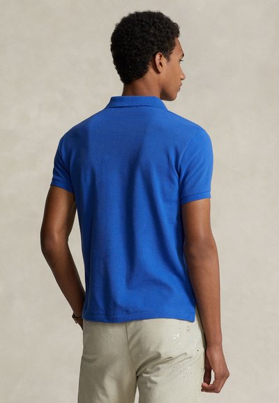 Ρουά μπλουζάκι πόλο με υφασμάτινη υφή, κοντά μανίκια και κλασικό γιακά, σε συνδυασμό με ανοιχτό μπεζ παντελόνι.