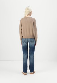 Hnědý pletený svetr s volným střihem a dlouhými rukávy, spárovaný s modrými džíny z denimu s mírným vyblednutím a rovnými nohavicemi.