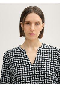 Blusa de estampado en blanco y negro con escote en V, que presenta un diseño geométrico de formas alternas, fabricada en tejido ligero y con un corte holgado.