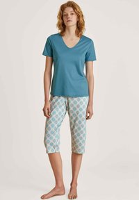 Teal V-hals T-shirt gecombineerd met gestreepte capri-broek in zachte pastelkleuren, met geometrische ontwerpen in blauw en beige. Over het geheel een gladde textuur.