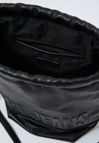 Borsa a secchiello in pelle nera con finitura strutturata e parte superiore arricciata. L'interno presenta una fodera in tessuto nero liscio e una piccola tasca con zip.