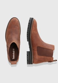 Hnědé kožené kotníkové boty s elastickými bočními panely, texturovanou gumovou podrážkou a poutkem na nazouvání. Mají zaoblený tvar špičky a jemné prošití.