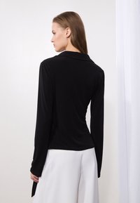 Black long-sleeve top with a smooth texture, tailored fit, and a classic collar, paired with white high-waisted trousers.