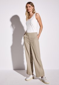 Beige wijde broek met zijzakken, gecombineerd met een witte tanktop en witte sneakers. Soepele textuur, strakke lijnen en casual pasvorm.