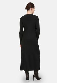 Robe noire à manches longues en côte, avec un corsage ajusté et une jupe évasée. Le matériau a une finition texturée, associée à des bottes brunes jusqu'aux genoux.