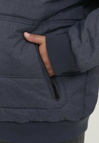 Mornarska podložena jakna z teksturirano tkanino, z zadrgo na strani in rebrastimi manšetami za tesno prileganje.