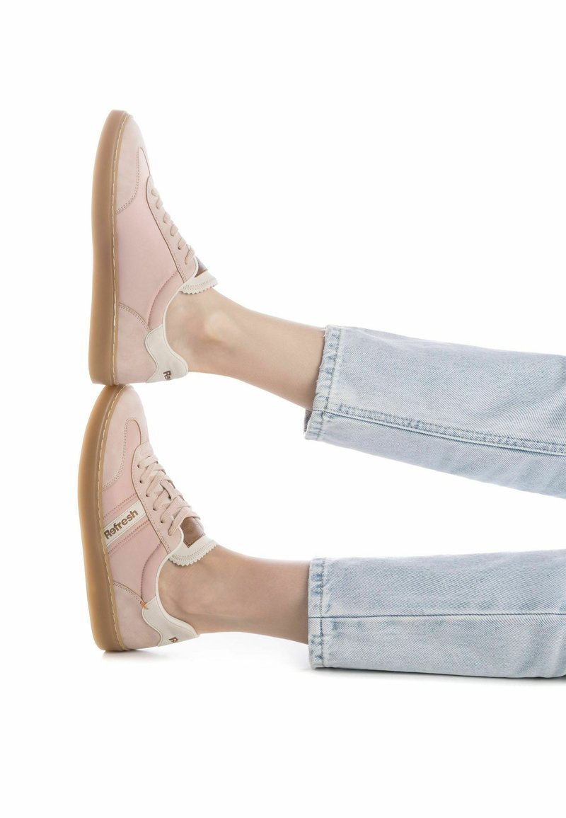 Zapatillas de deporte rosa claro con acentos en beige, diseño con cordones y suela de goma. Presentan un detalle de logo en el lateral y un talón texturizado.