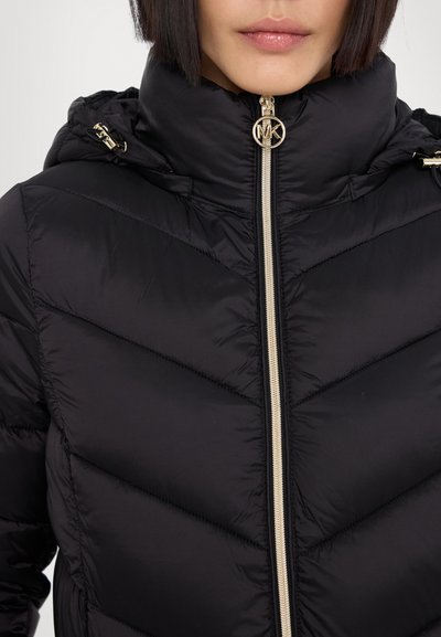 Doudoune noire avec un col haut, des coutures en chevron, des éléments en métal doré et une fermeture à glissière avec logo. Tissu lisse et brillant avec une finition texturée.